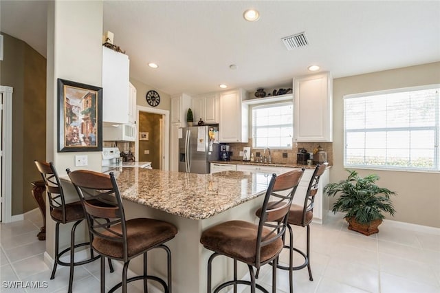 kitchen with a peninsula, stove, visible vents, stainless steel refrigerator with ice dispenser, and decorative backsplash