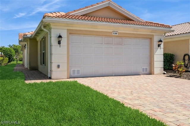 view of front of house featuring an attached garage, a tiled roof, decorative driveway, stucco siding, and a front lawn