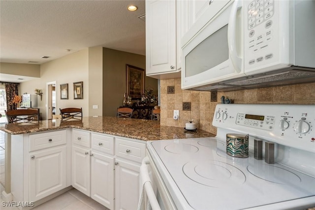 kitchen featuring dark stone counters, white appliances, white cabinets, and a peninsula