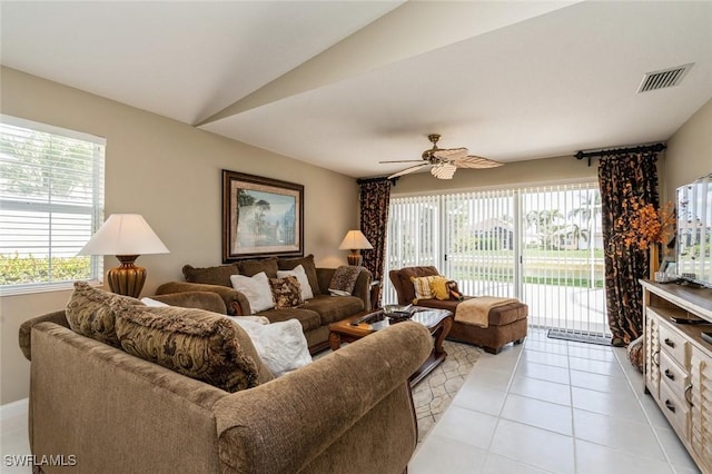 living area featuring lofted ceiling, light tile patterned floors, ceiling fan, and visible vents