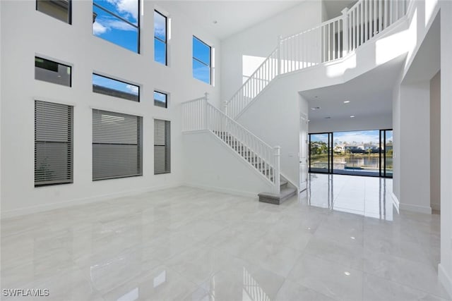 unfurnished living room featuring stairway, plenty of natural light, and baseboards