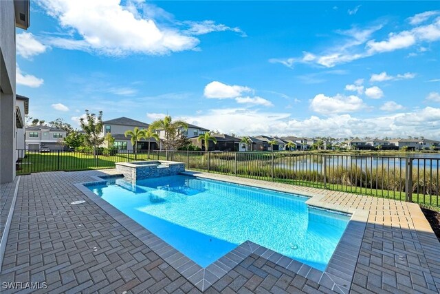 view of pool featuring a water view, a pool with connected hot tub, a patio, fence, and a residential view