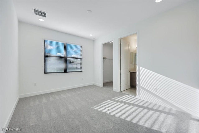 unfurnished bedroom featuring a spacious closet, light colored carpet, visible vents, and baseboards