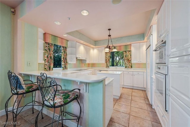 kitchen with light countertops, hanging light fixtures, white cabinetry, a peninsula, and a kitchen bar