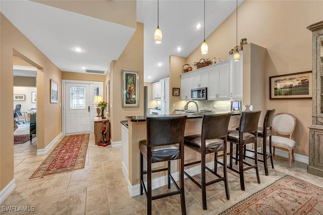 kitchen featuring dark countertops, stainless steel microwave, white cabinets, a peninsula, and a kitchen bar