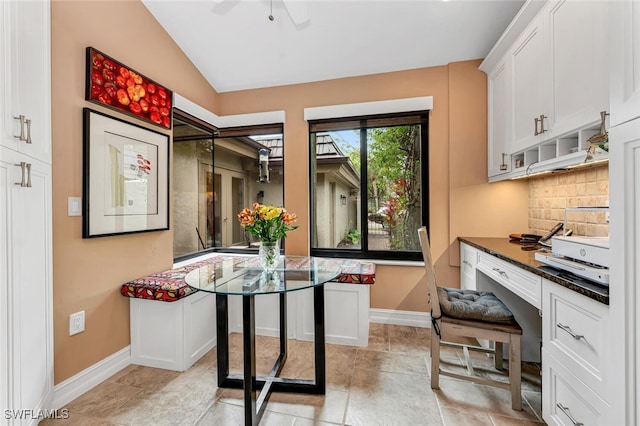 kitchen featuring lofted ceiling, decorative backsplash, built in study area, white cabinets, and baseboards