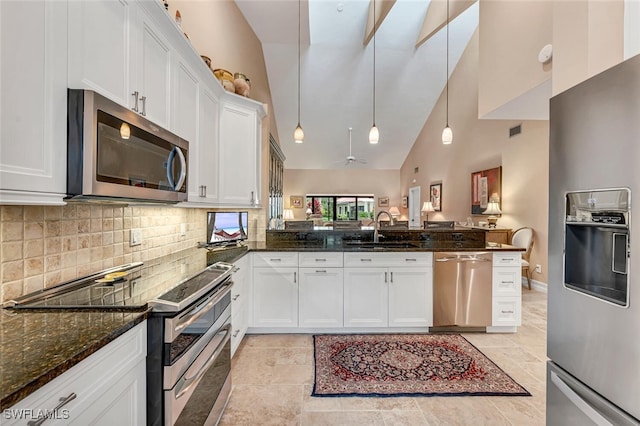 kitchen featuring a peninsula, a sink, white cabinets, appliances with stainless steel finishes, and dark stone counters