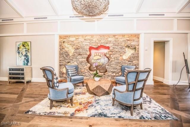 living area with visible vents, beamed ceiling, baseboards, and wood finished floors