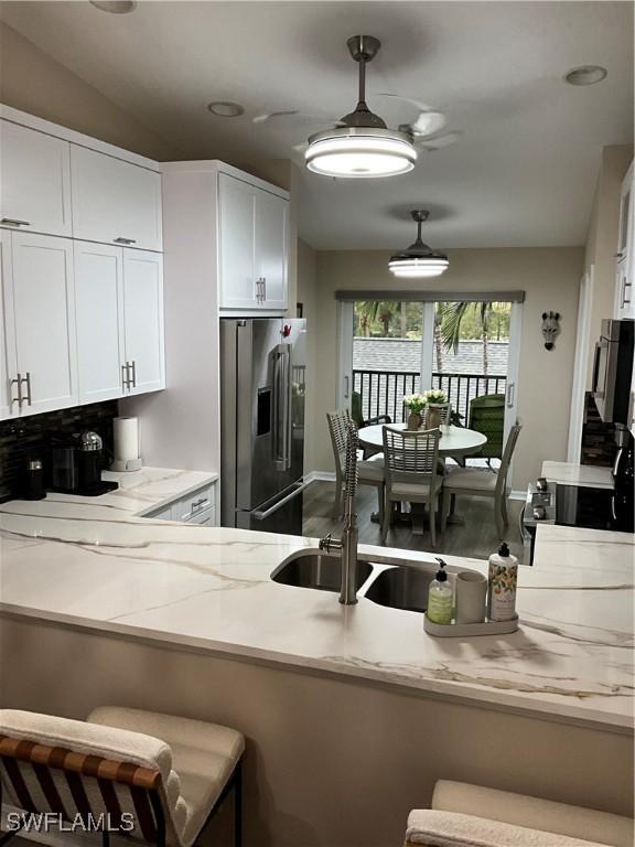 kitchen with white cabinets, light stone counters, a breakfast bar, decorative light fixtures, and high end fridge