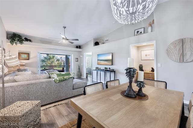 dining space with high vaulted ceiling, ceiling fan with notable chandelier, and wood finished floors