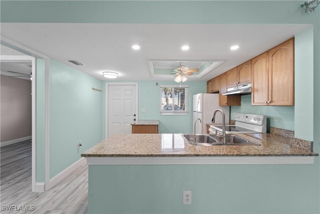 kitchen featuring under cabinet range hood, a tray ceiling, white appliances, a peninsula, and baseboards