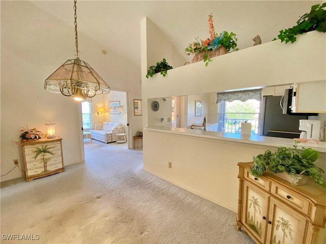 interior space featuring pendant lighting, light countertops, stainless steel microwave, a towering ceiling, and light carpet