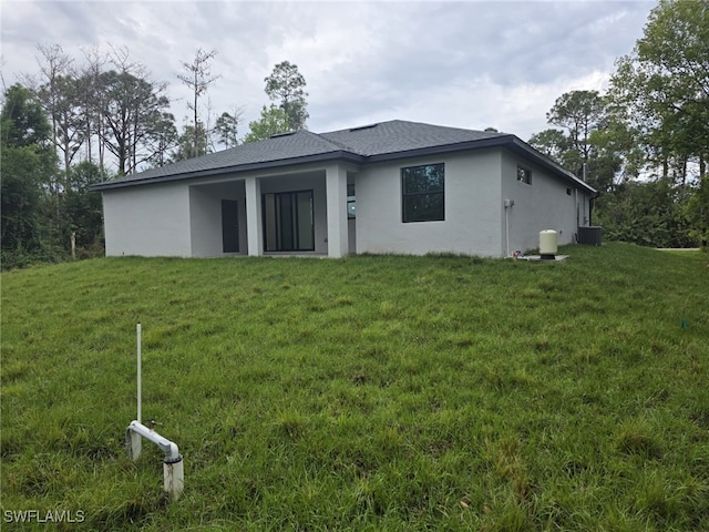 back of property featuring a yard, a shingled roof, central AC, and stucco siding