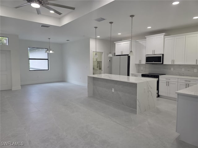 kitchen featuring a kitchen island, appliances with stainless steel finishes, open floor plan, decorative light fixtures, and white cabinetry