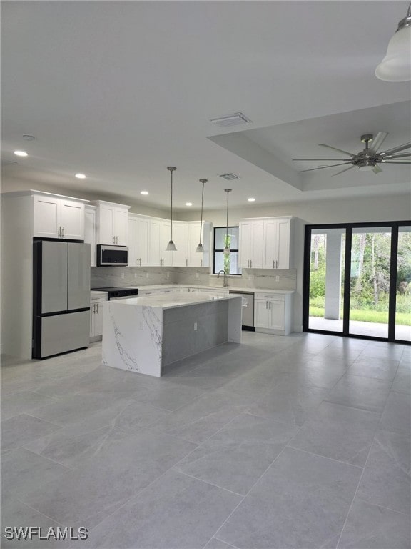 kitchen with appliances with stainless steel finishes, open floor plan, a center island, white cabinetry, and pendant lighting