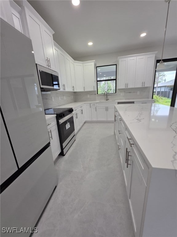 kitchen with electric range, white cabinets, freestanding refrigerator, stainless steel microwave, and decorative light fixtures