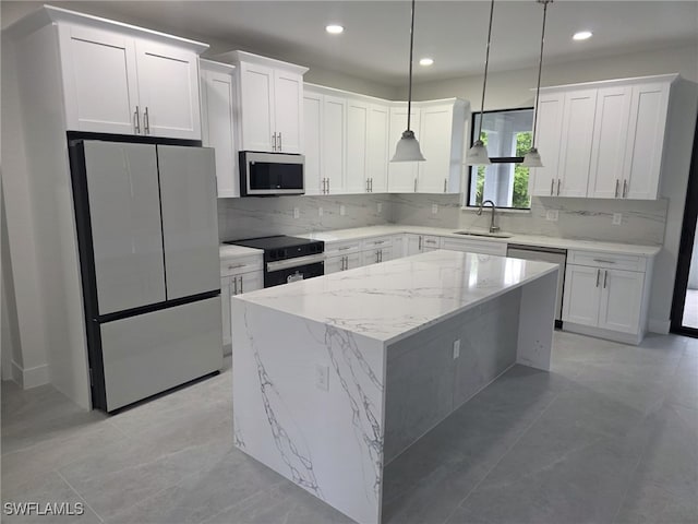 kitchen with hanging light fixtures, appliances with stainless steel finishes, white cabinets, a sink, and a kitchen island