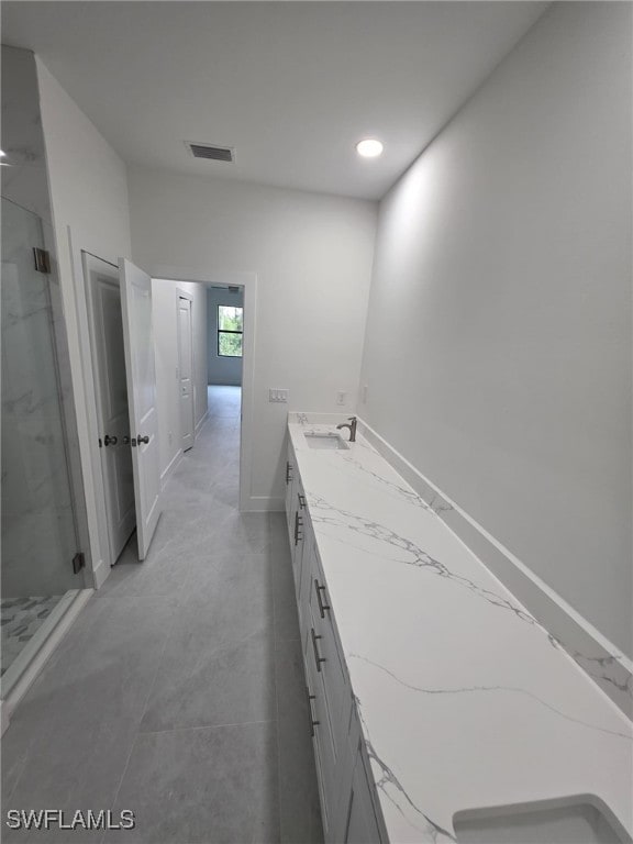 bathroom with a marble finish shower, double vanity, visible vents, a sink, and baseboards