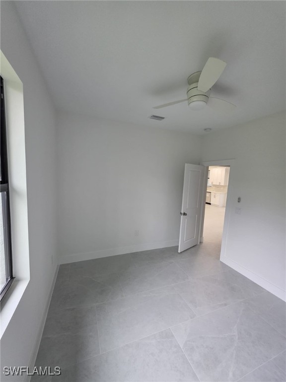 empty room featuring ceiling fan, visible vents, and baseboards