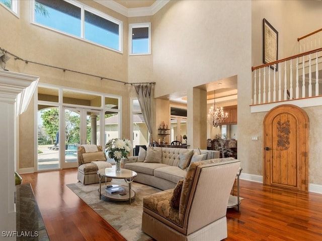 living area with baseboards, wood finished floors, an inviting chandelier, crown molding, and french doors