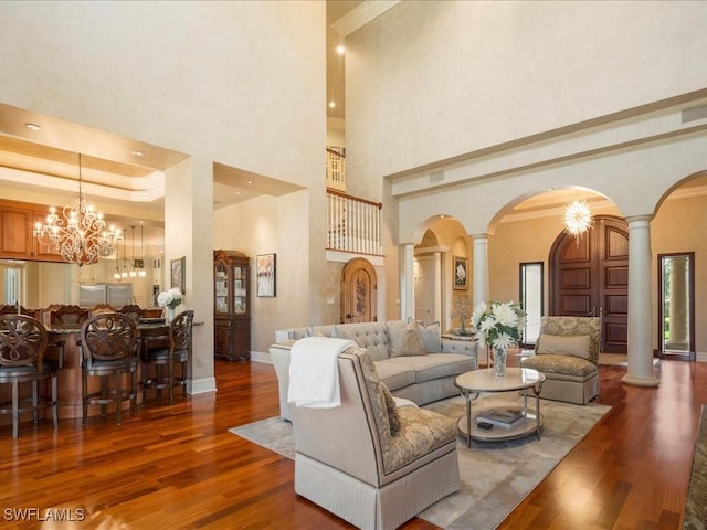 living area featuring dark wood-style floors, a tray ceiling, decorative columns, and baseboards