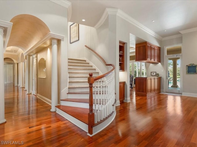 stairs featuring arched walkways, wood finished floors, baseboards, ornamental molding, and ornate columns