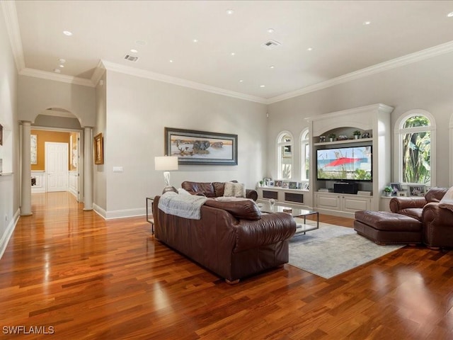 living area with arched walkways, wood finished floors, baseboards, ornamental molding, and decorative columns