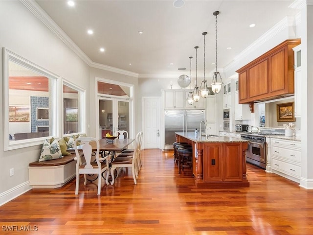 kitchen featuring brown cabinetry, high quality appliances, a kitchen breakfast bar, decorative light fixtures, and a kitchen island with sink