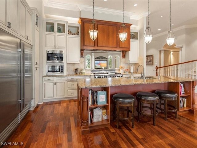 kitchen with pendant lighting, a sink, an island with sink, and built in appliances