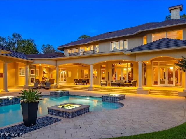 back of house featuring an outdoor living space with a fire pit, a patio, a chimney, stucco siding, and a pool with connected hot tub