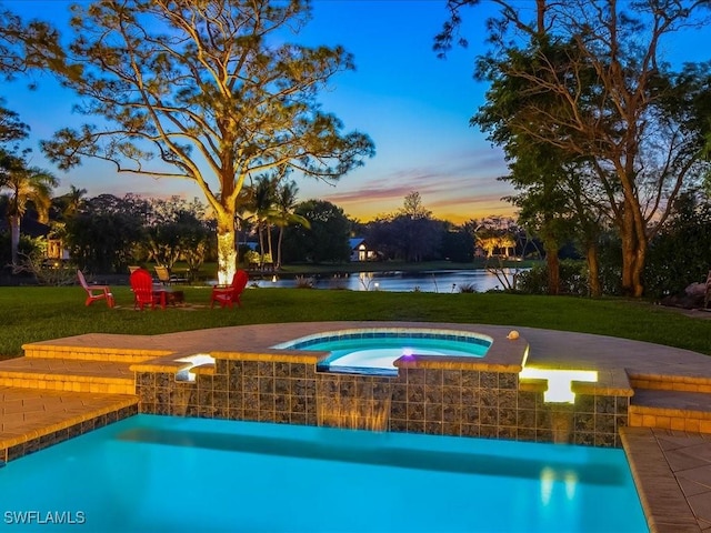 pool at dusk with an in ground hot tub, a yard, a water view, and an outdoor pool