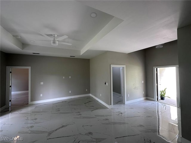 empty room with marble finish floor, a raised ceiling, and baseboards