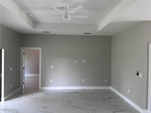 spare room featuring a tray ceiling, marble finish floor, visible vents, and baseboards