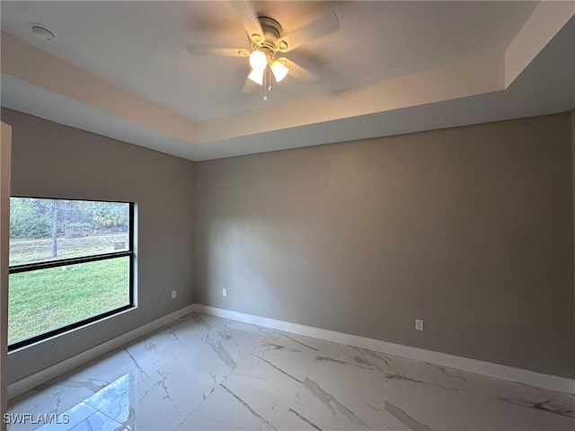 empty room featuring marble finish floor, a raised ceiling, ceiling fan, and baseboards