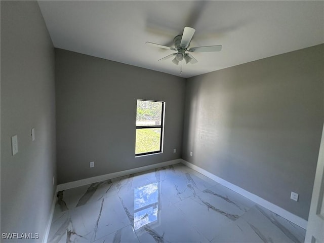 empty room featuring marble finish floor, a ceiling fan, and baseboards