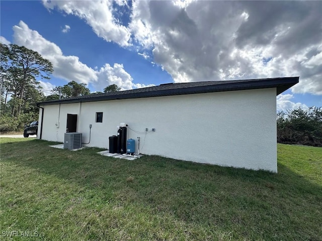 rear view of house featuring central AC, a lawn, and stucco siding