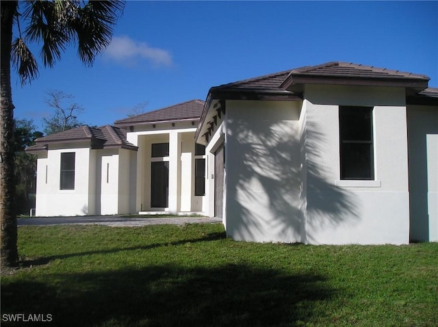 exterior space with stucco siding, a tile roof, and a yard