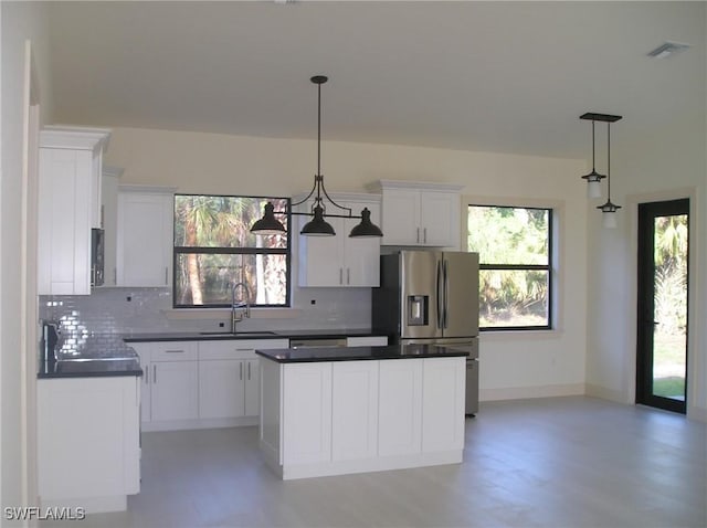 kitchen featuring a sink, backsplash, a wealth of natural light, dark countertops, and stainless steel fridge