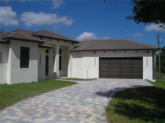 prairie-style house featuring a garage, decorative driveway, a tile roof, and stucco siding