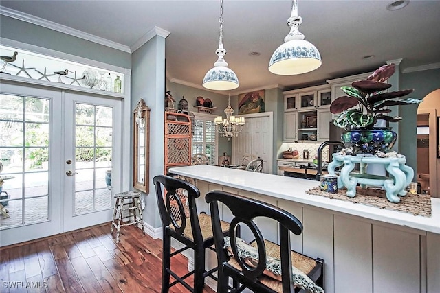 kitchen featuring french doors, decorative light fixtures, dark wood finished floors, glass insert cabinets, and ornamental molding