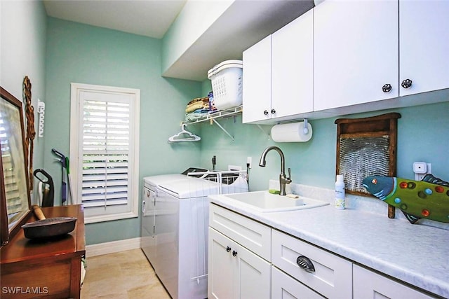 laundry area featuring washing machine and clothes dryer, cabinet space, a sink, light wood-type flooring, and baseboards