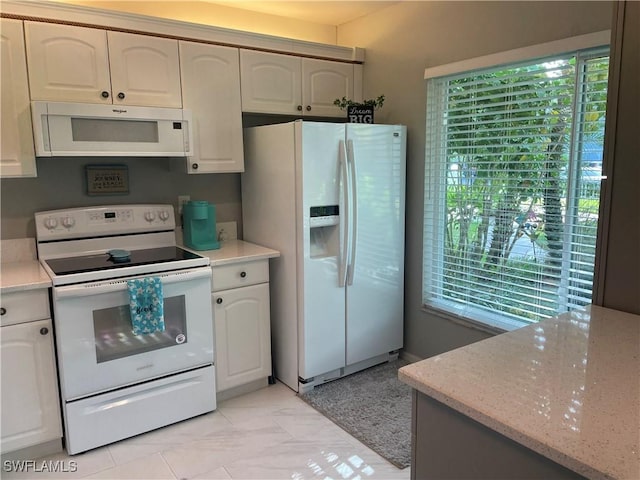 kitchen featuring light stone counters, a wealth of natural light, white appliances, and white cabinetry