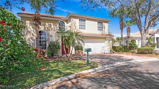 mediterranean / spanish house featuring an attached garage, a tiled roof, decorative driveway, and stucco siding