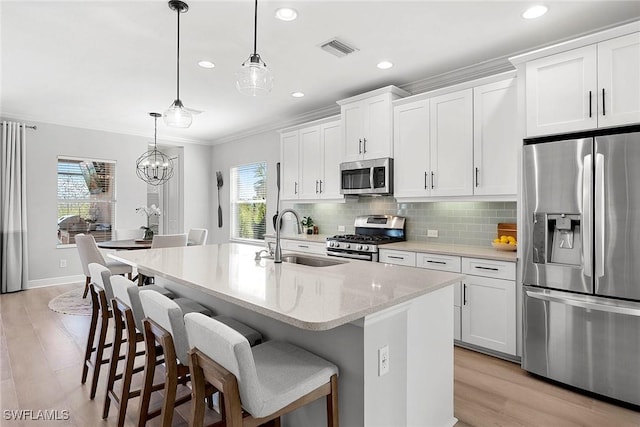 kitchen featuring stainless steel appliances, a center island with sink, white cabinetry, and decorative light fixtures