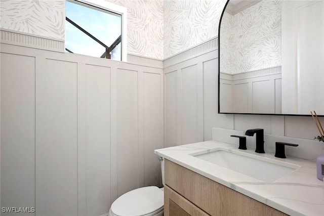 bathroom with toilet, a decorative wall, and vanity