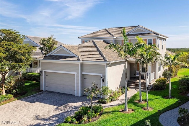 view of front facade featuring an attached garage, a tiled roof, decorative driveway, stucco siding, and a front yard