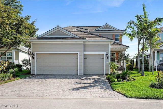 view of front of home featuring a garage, decorative driveway, a tiled roof, and a front lawn