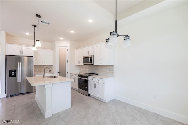 kitchen with a kitchen island with sink, white cabinetry, light countertops, appliances with stainless steel finishes, and pendant lighting