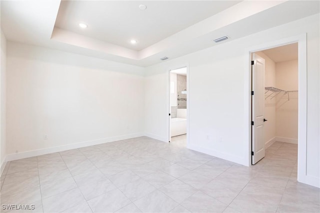 unfurnished bedroom featuring a walk in closet, recessed lighting, a raised ceiling, visible vents, and baseboards