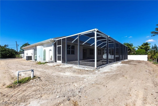 rear view of property featuring glass enclosure, central AC unit, fence, and stucco siding